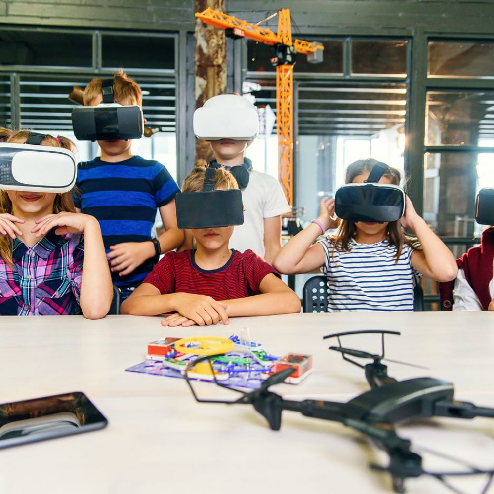 Innovative young generation future technology. Group of six school children wearing virtual reality glasses with raised arms work on new programing project during the lesson in smart modern school.